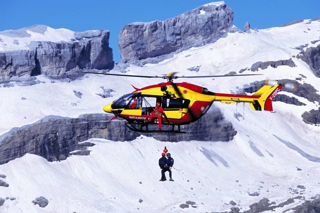Rescuer and victim hang below a helicopter on a rope during a heli-lift  over a snowy mountain.