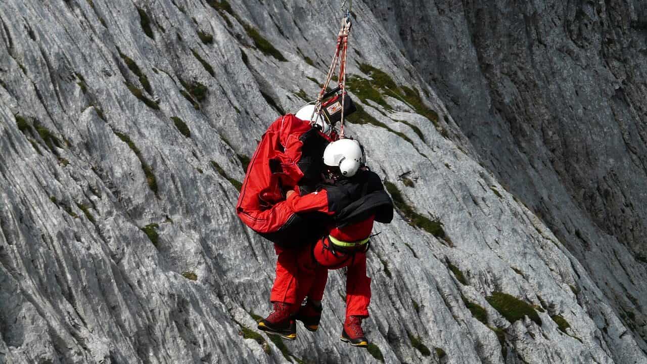 Two rescuers attached to a rope practice a helicopter rescue in the Alps