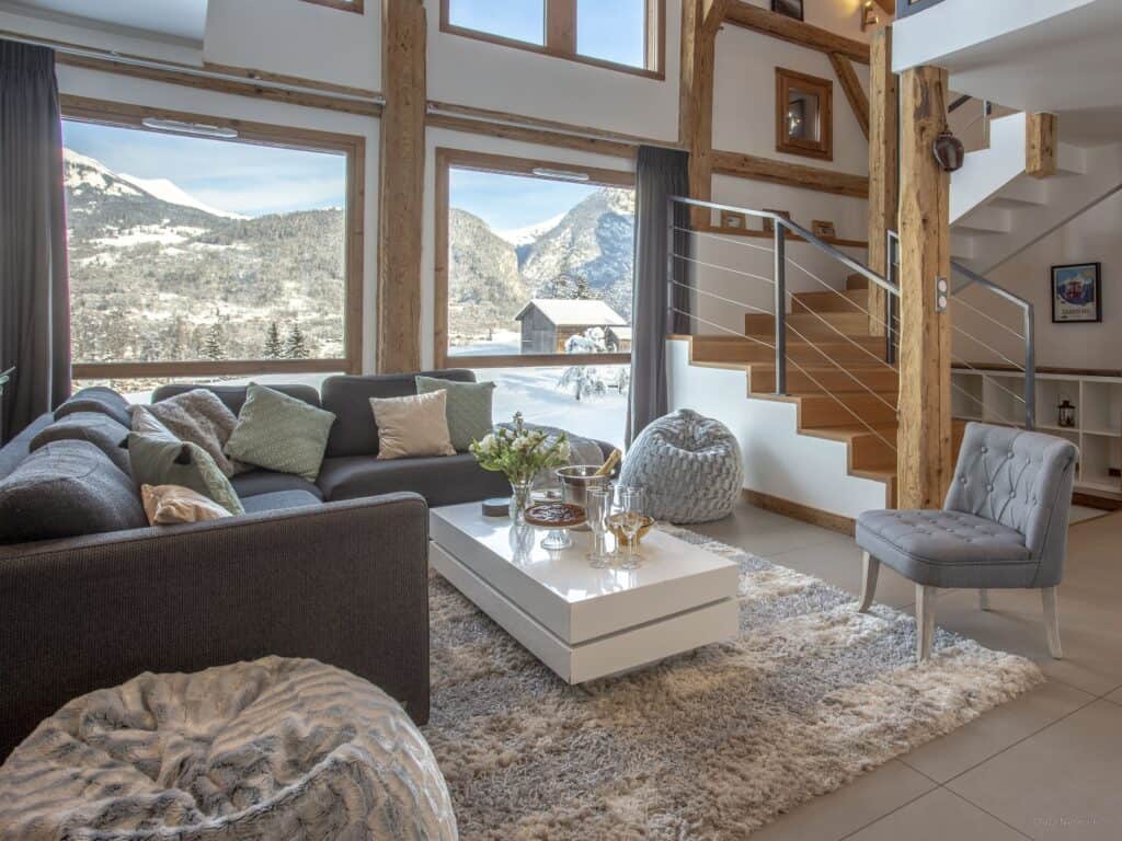 A light-filled living room with an L-shaped sofa, a chair and floor cushions with a view to the mountains