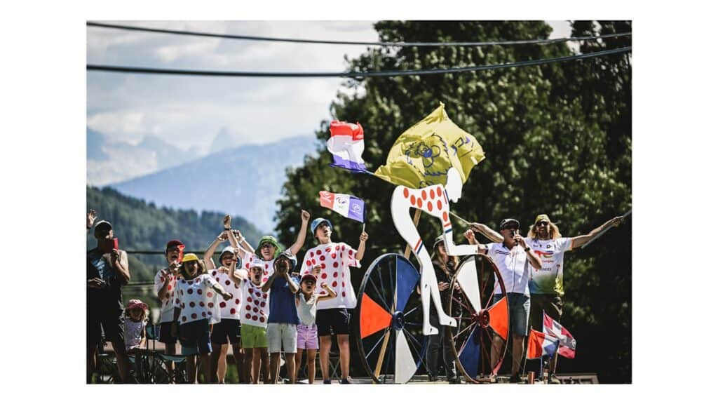 Crowds dressed in polka dot shirts with a model of a cyclist on the side of the Tour de France route