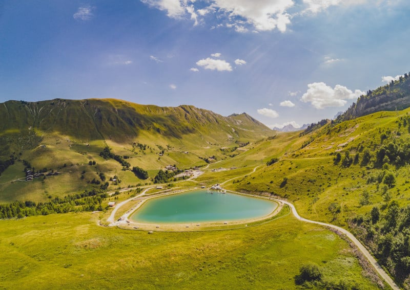 Lac turquoise entouré de montagnes vertes, sous un ciel bleu.