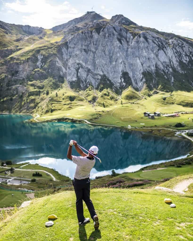 Golfeur frappant la balle face à un lac et des montagnes.