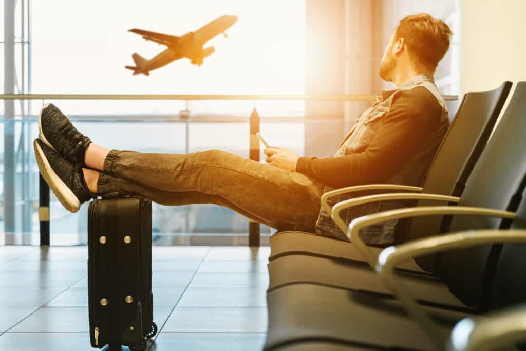 Un homme assis dans un aéroport, les jambes posées sur ses bagages, regardant un avion.