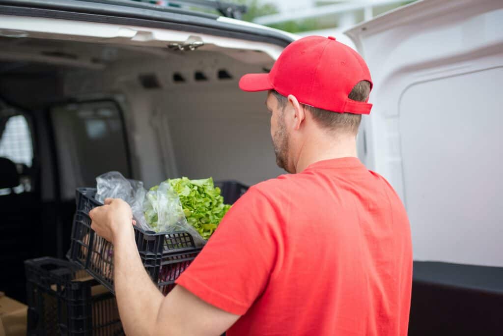 A delivery driver lifts a tray of salad out of his van