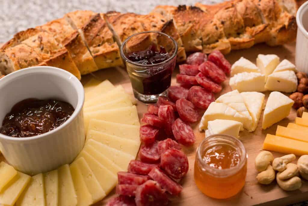 A wooden aperitif board with cheese, sausage, bread, honey, nuts and preserves