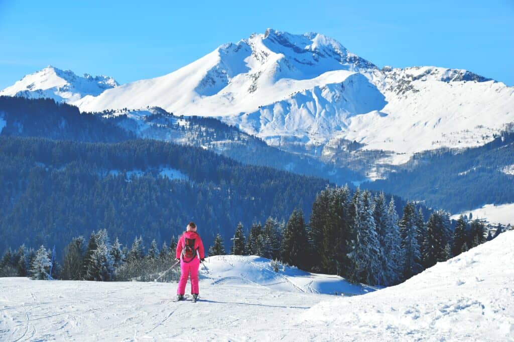Une femme en tenue de ski rose descend une piste enneigée. 