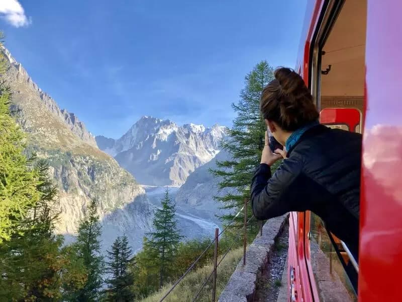 Femme prenant une photo des montagnes enneigées depuis un train rouge.