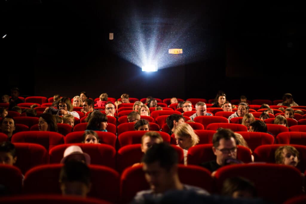 Au cinéma de Méribel, dans les 3 Vallées, les spectateurs assis dans des fauteuils rouges regardent un film au cinéma. Au fond de la salle, une lumière vive sort de la cabine de projection. 