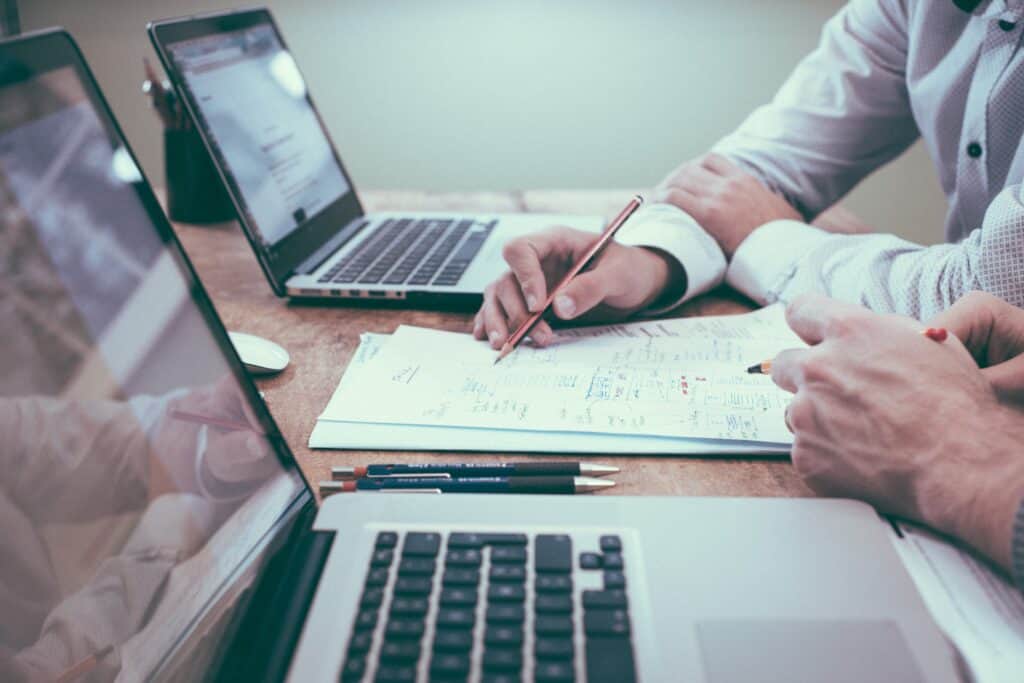Two people working on a property investment project with computers and paper documents. 