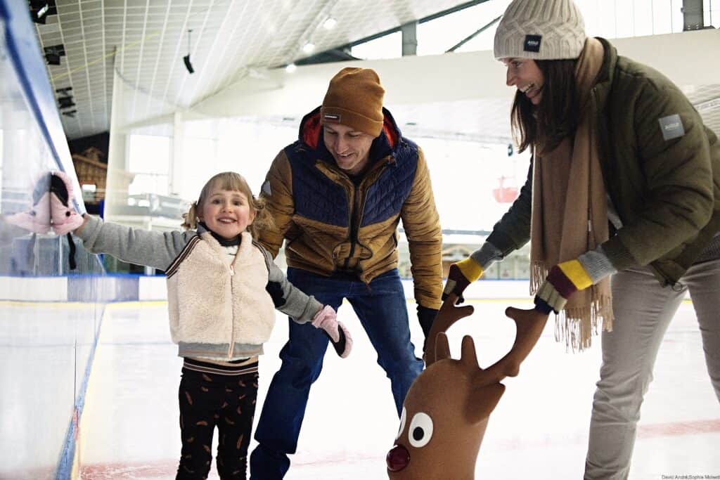A la patinoire de Courchevel dans les 3 Vallées, une enfant souriante patine en compagnie de ses parents et d'une mascotte.
