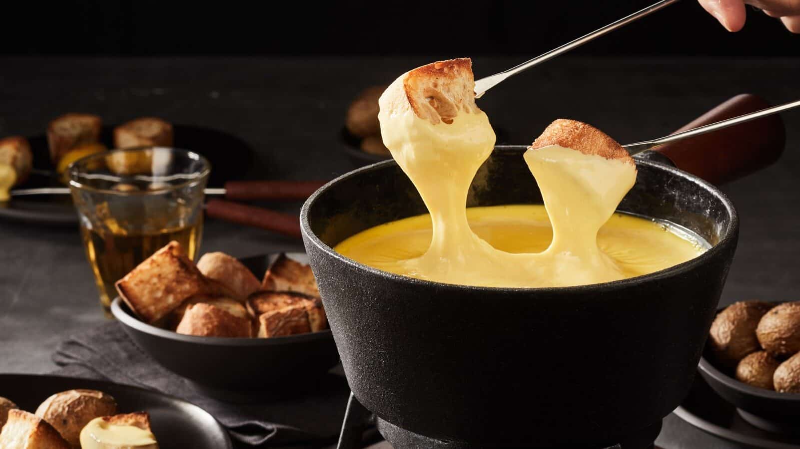 Two pieces of bread are dipped into a fondue pot of melted cheese