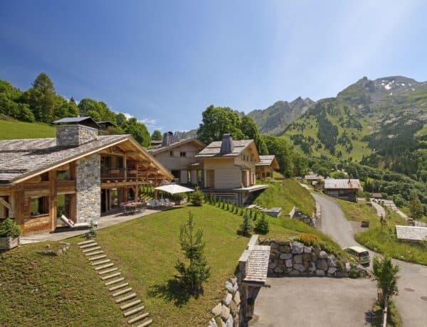 Extérieur du Lodge Fauspe à La Clusaz fait de pierres et de bois, avec sa terrasse et ses transats.