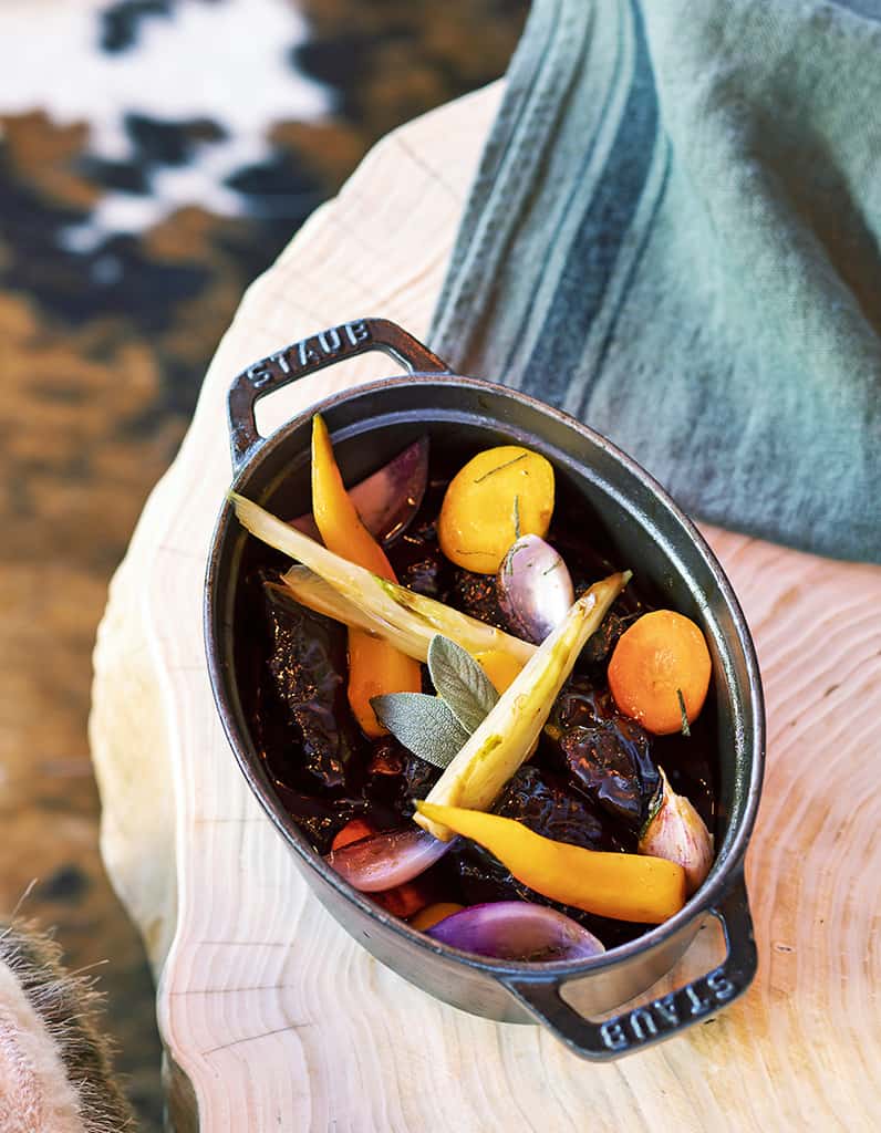 A bottle of wine and a pot of beef cheeks cooked in red wine