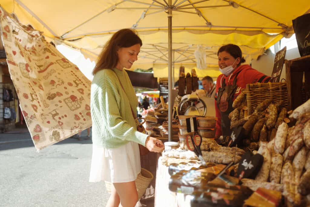 Une femme demande un échantillon d'une spécialité locale dans un marché alpin. 