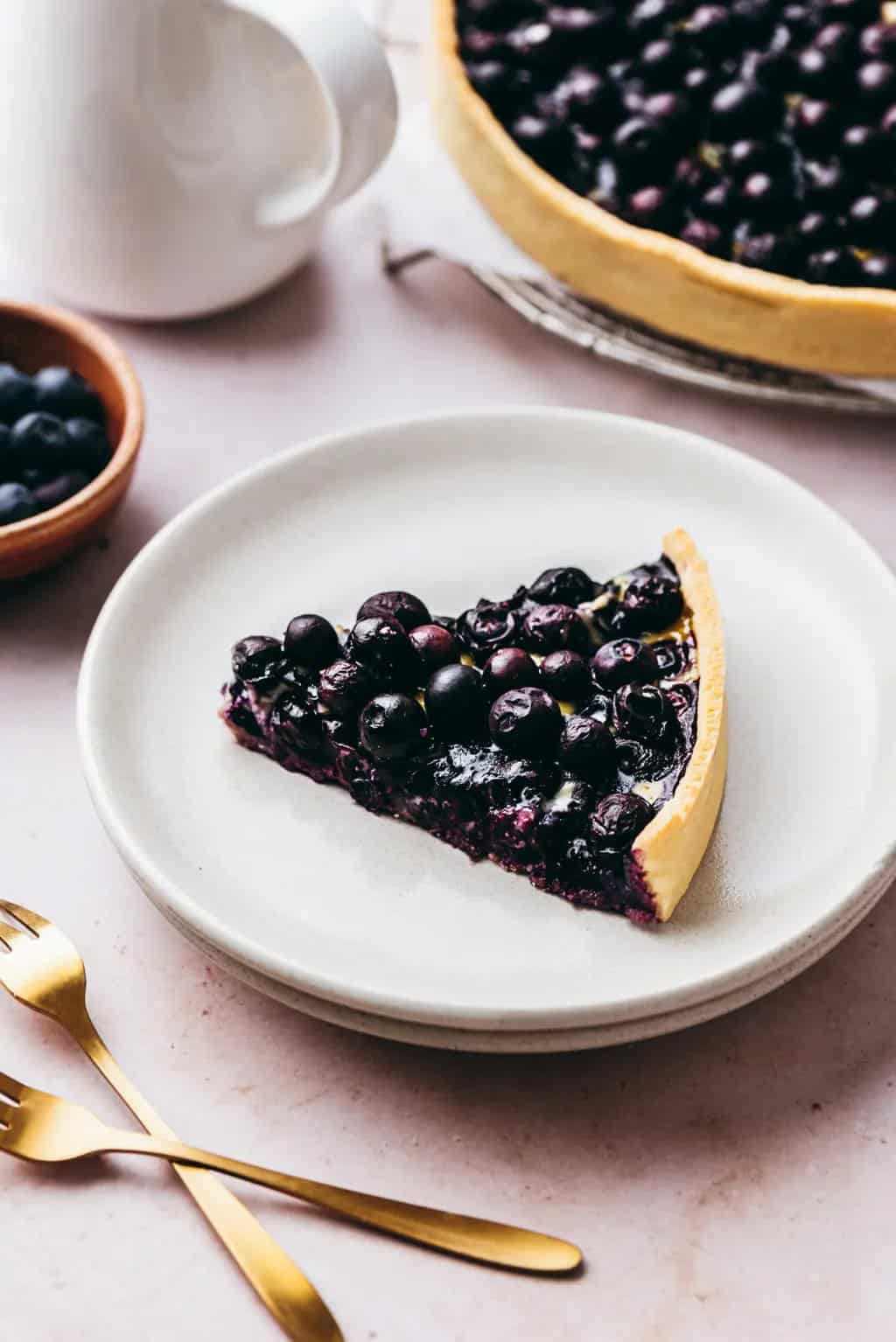 A slice of bilberry tart on a white place with two golden dessert forks
