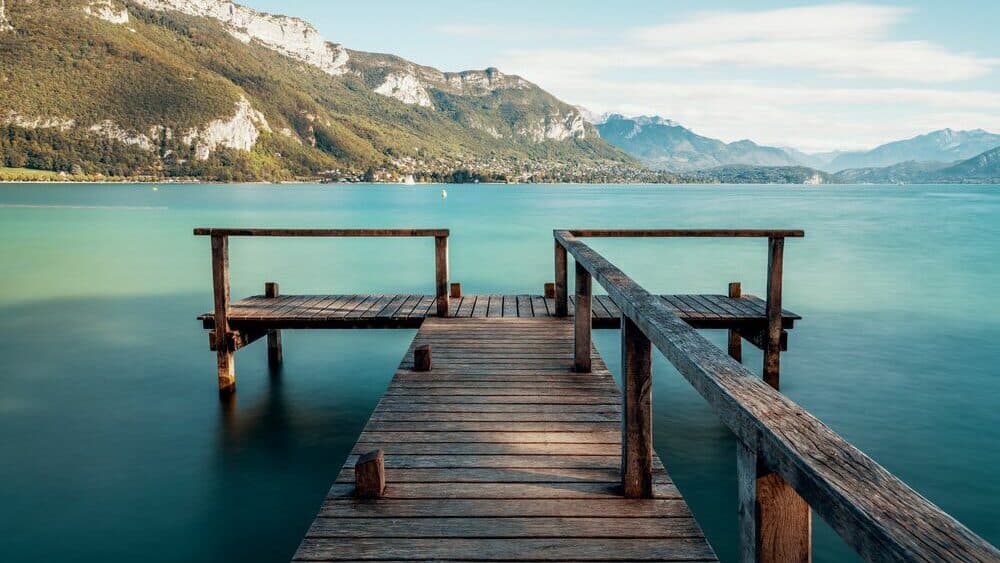 A wooden pontoon on lake Annecy surrounded by turquoise waters and green mountainsides