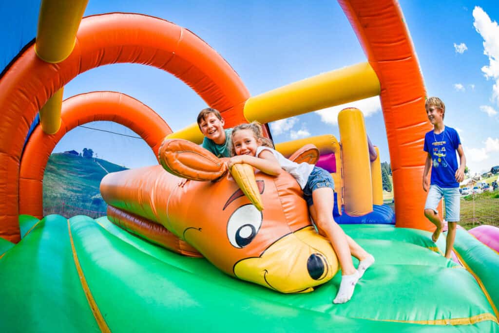 Three kids playing on a colourful inflatable castle, one of the best activities for family holidays in the Alps.
