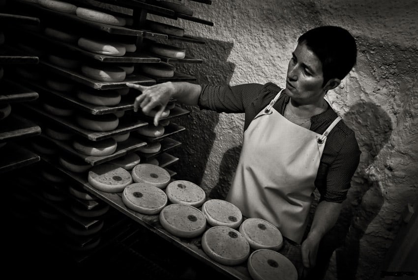 A woman in a white apron checks the reblochon cheeses in the maturing cellar
