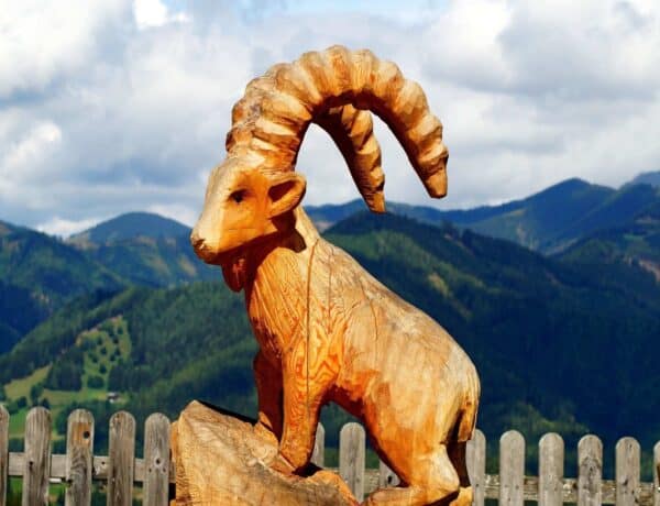 Une sculpture de chamois en bois sur son promontoire, avec les montagnes en arrière-plan.