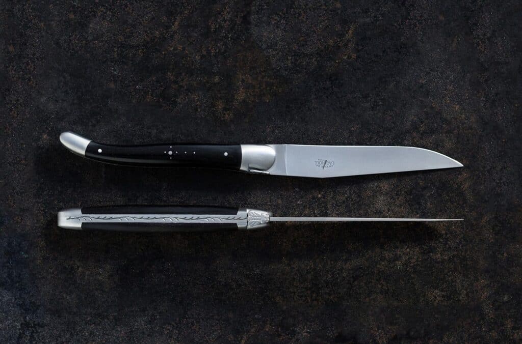 Laguiole knives with black handles, set on a black and brown surface.
