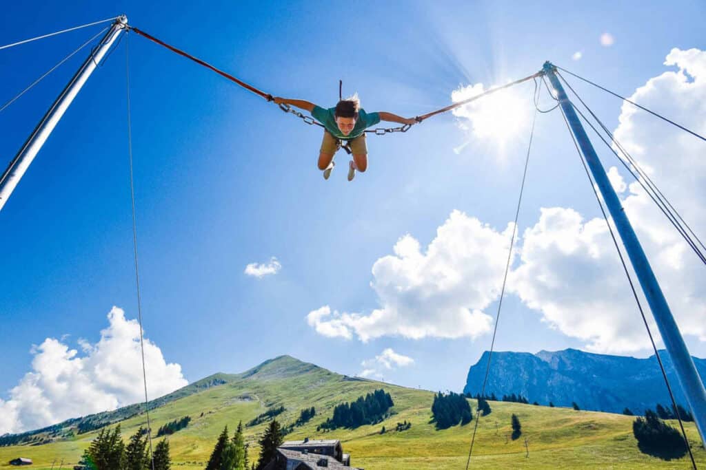 Teenager on a trampoline, with the sky and mountains in the background.