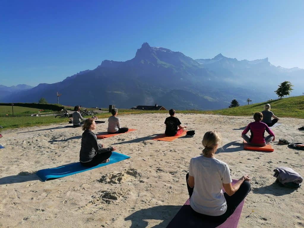 Des personnes pratiquant le yoga sur leur tapis dans le sable, face aux montagnes.