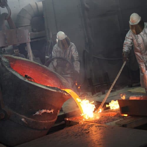 Men dressed in protective suits and headgear pour red-hot molten metal