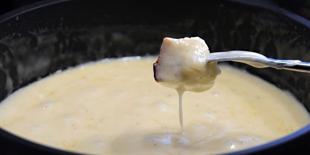 A piece of bread dripping with melted cheese is lifted from the fondue pot