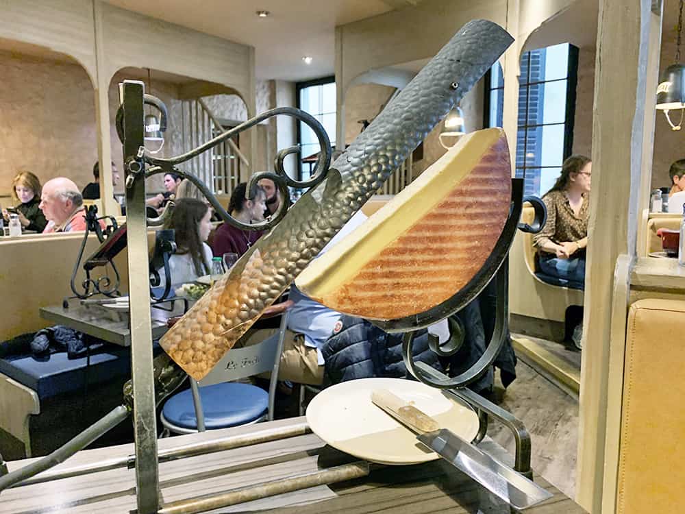 A half wheel of raclette cheese sits on a traditional heating device