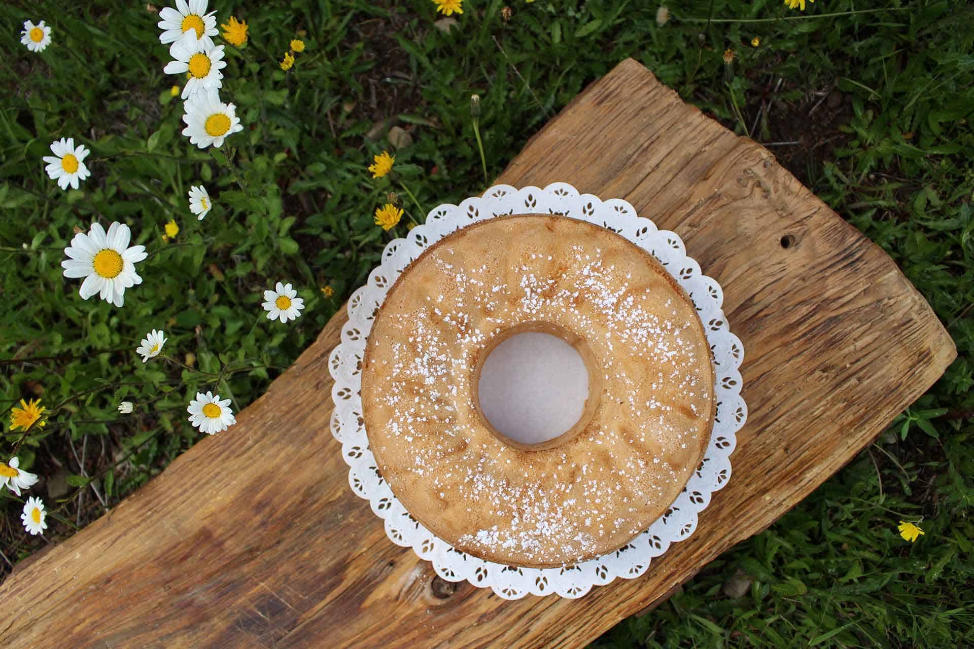 A gâteau de Savoie in a lace doily on a plank of wood on the grass