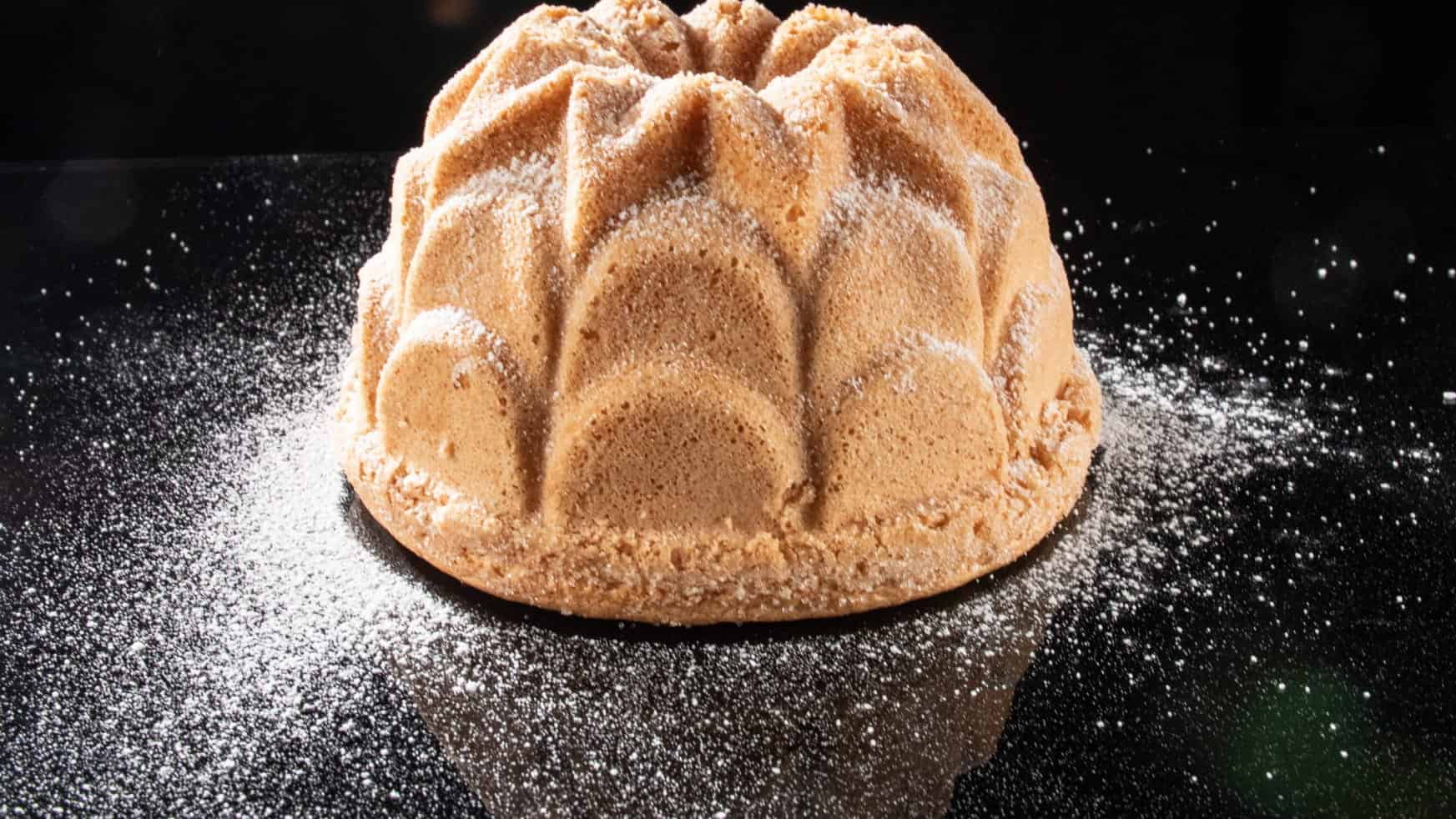 A Gâteau de Savoie dusted with icing sugar on a black surface
