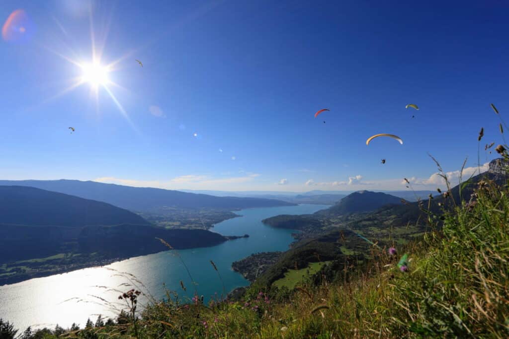 Paragliders soar over Lake Annecy in summer against a blue sky