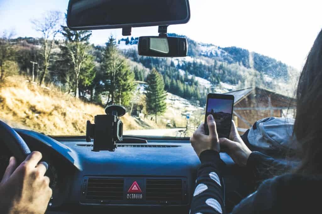 Deux personnes dans une voiture : l'une conduit et l'autre prend le paysage de montagnes en photo.