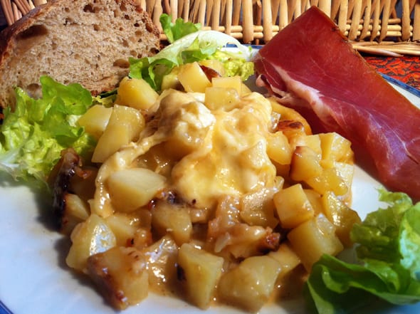 A dish of potatoes, cold meats and cheese, served with salad and bread.