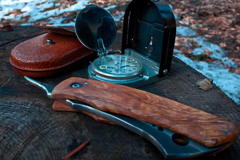 A folding knife next to a compass and a leather case
