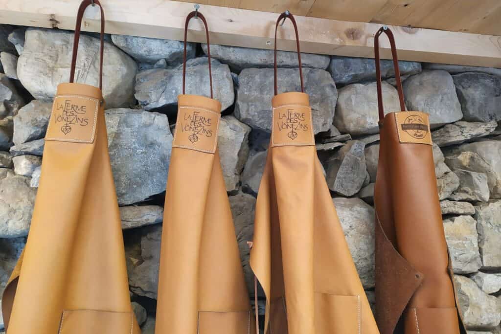 Four leather aprons hanging on hooks against a stone wall