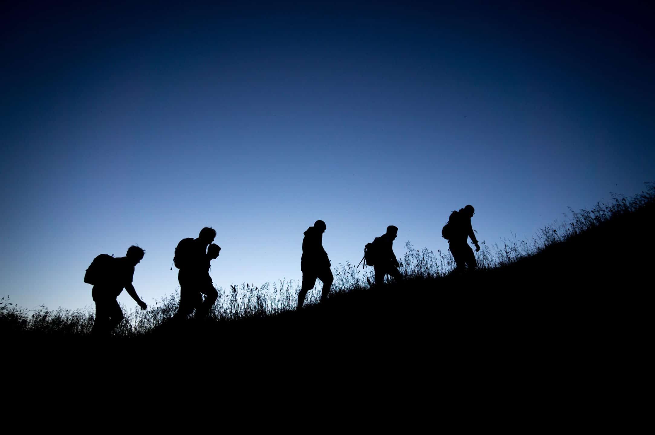 5 randonneurs marchant de nuit. On aperçoit juste leurs silhouettes dans la pénombre.