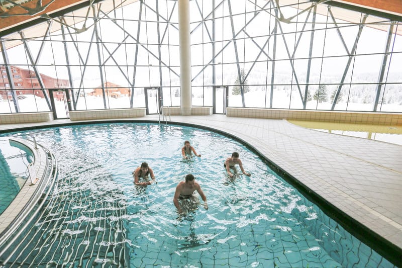 4 people ride aqua bikes in an indoor swimming pool