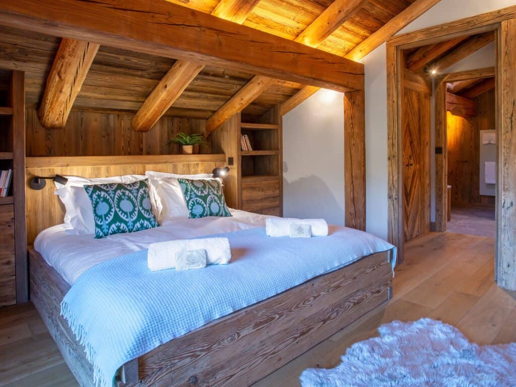 A double bed in a chalet with white linen and bath towels rolled up