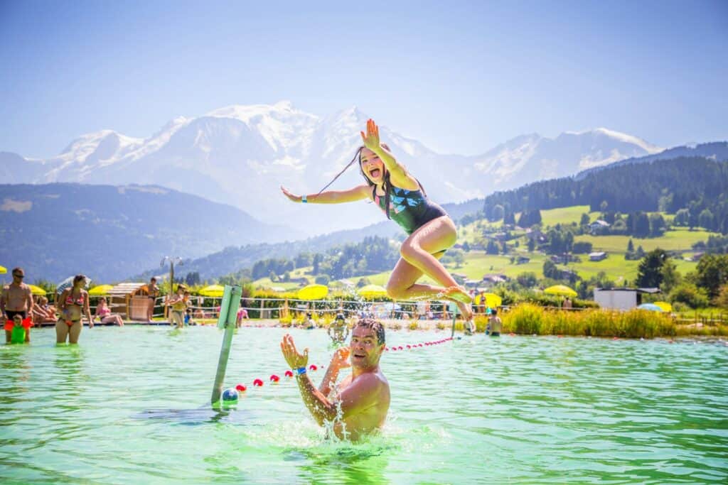 Une petite fille en train de sauter dans une piscine avec les montagnes en fond.
