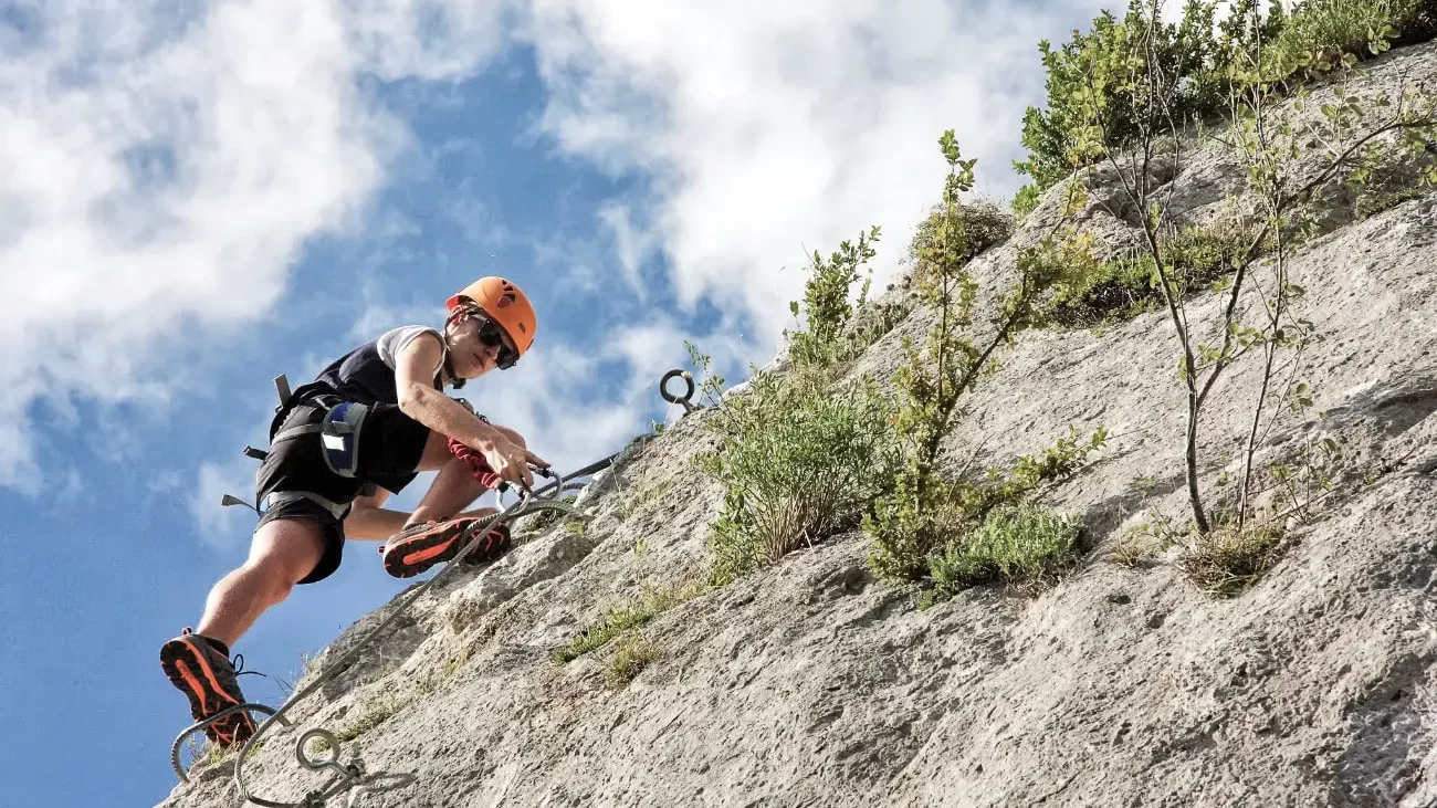 A man, equipped with a helmet and climbing gear, climbs to the top of a rock face in the Alps.