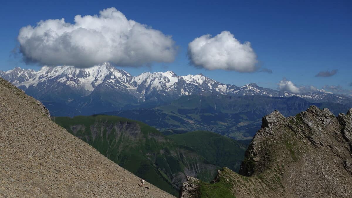A view of the Aravis mountains from a rocky cliff face - two white clouds hang in a blue sky
