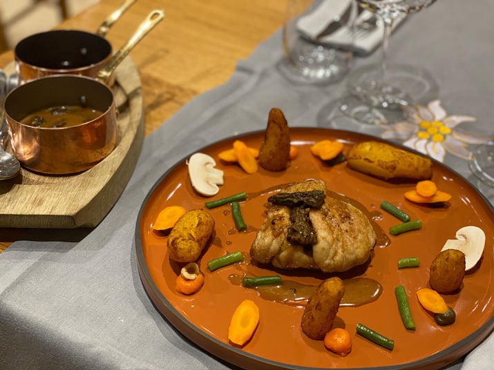 Un plat de viande avec des légumes dans un plat couleur terracotta. 