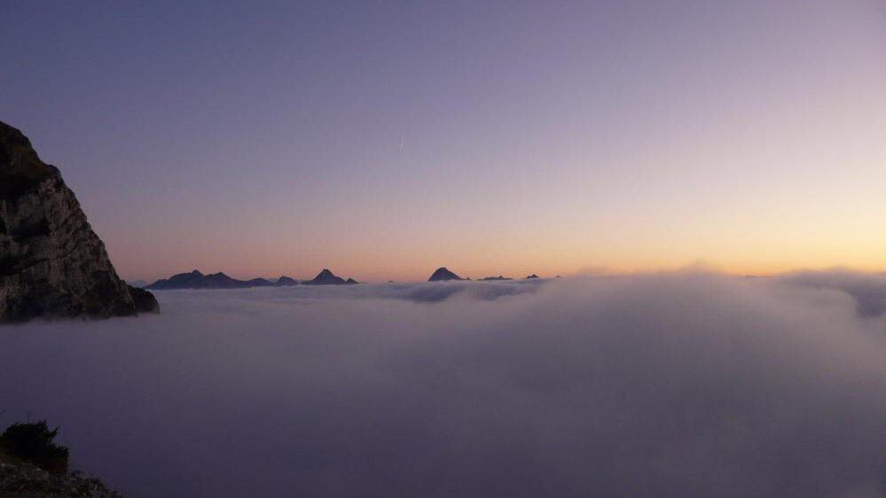 The sun rises through a blanket of clouds hanging over the Aravis mountains