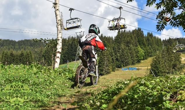 A child rides a moto cross in the grass as a chairlift passes overhead