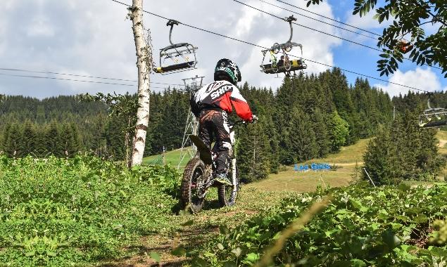 Un enfant sur une moto cross dans l'herbe avec des télésièges en arrière-plan.