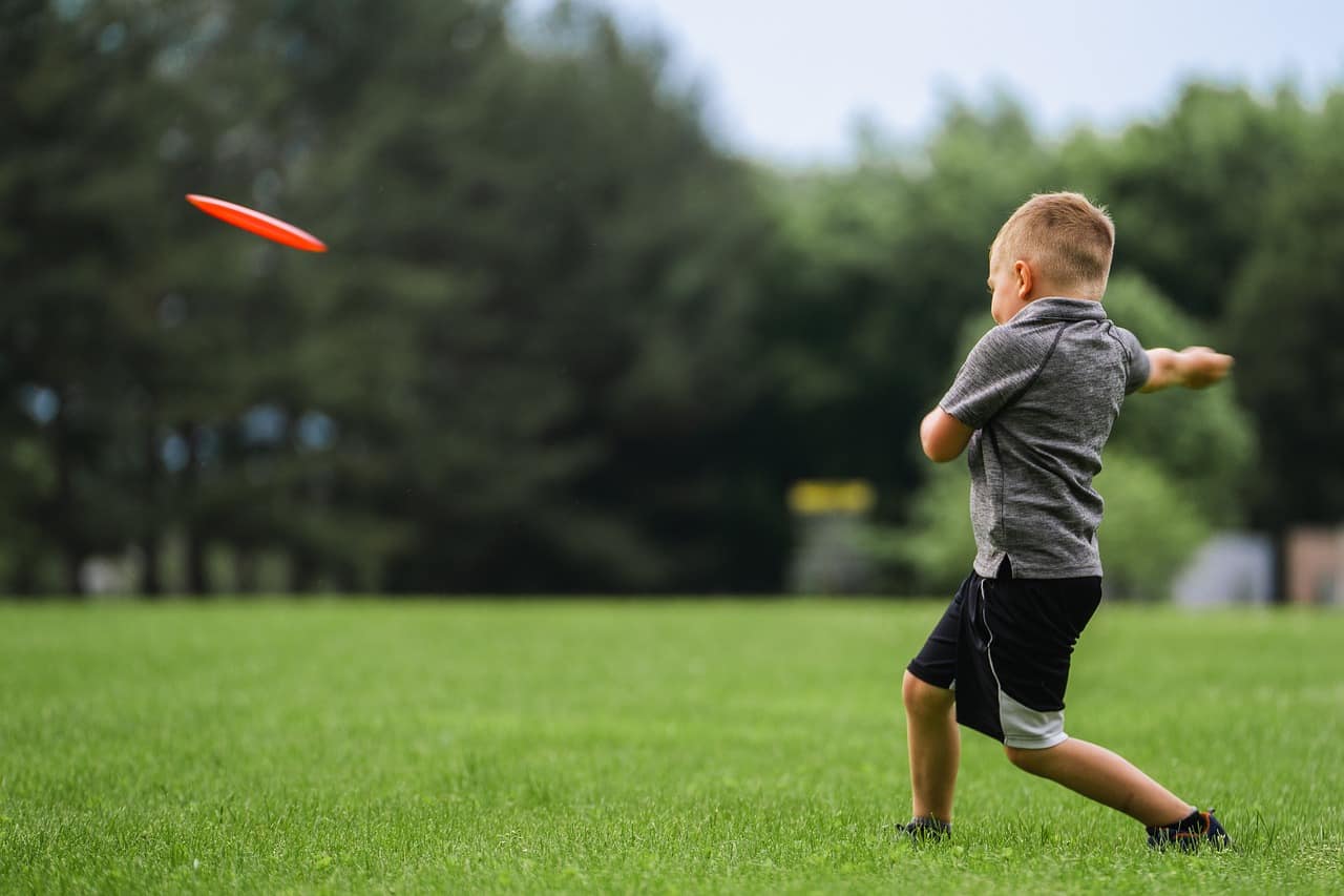 A young boy throws a frisbee on the grass