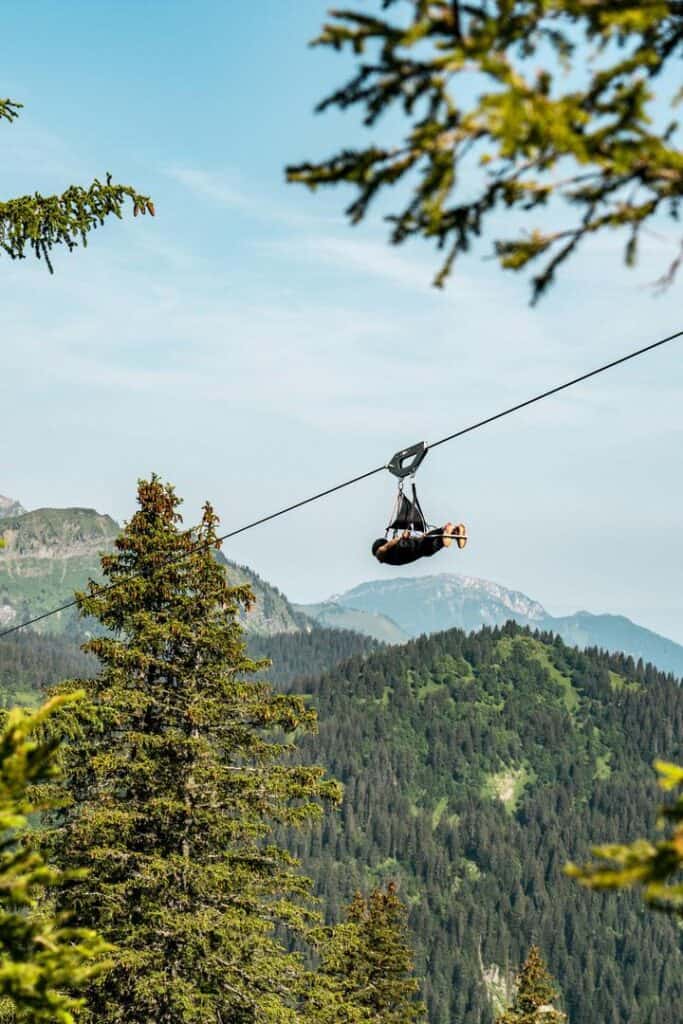 A person attached to a cable in the air flies between the trees in the middle of the mountains.