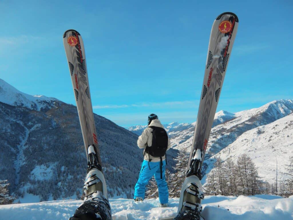 A view of a pair of skis framing another skier against a mountain landscape