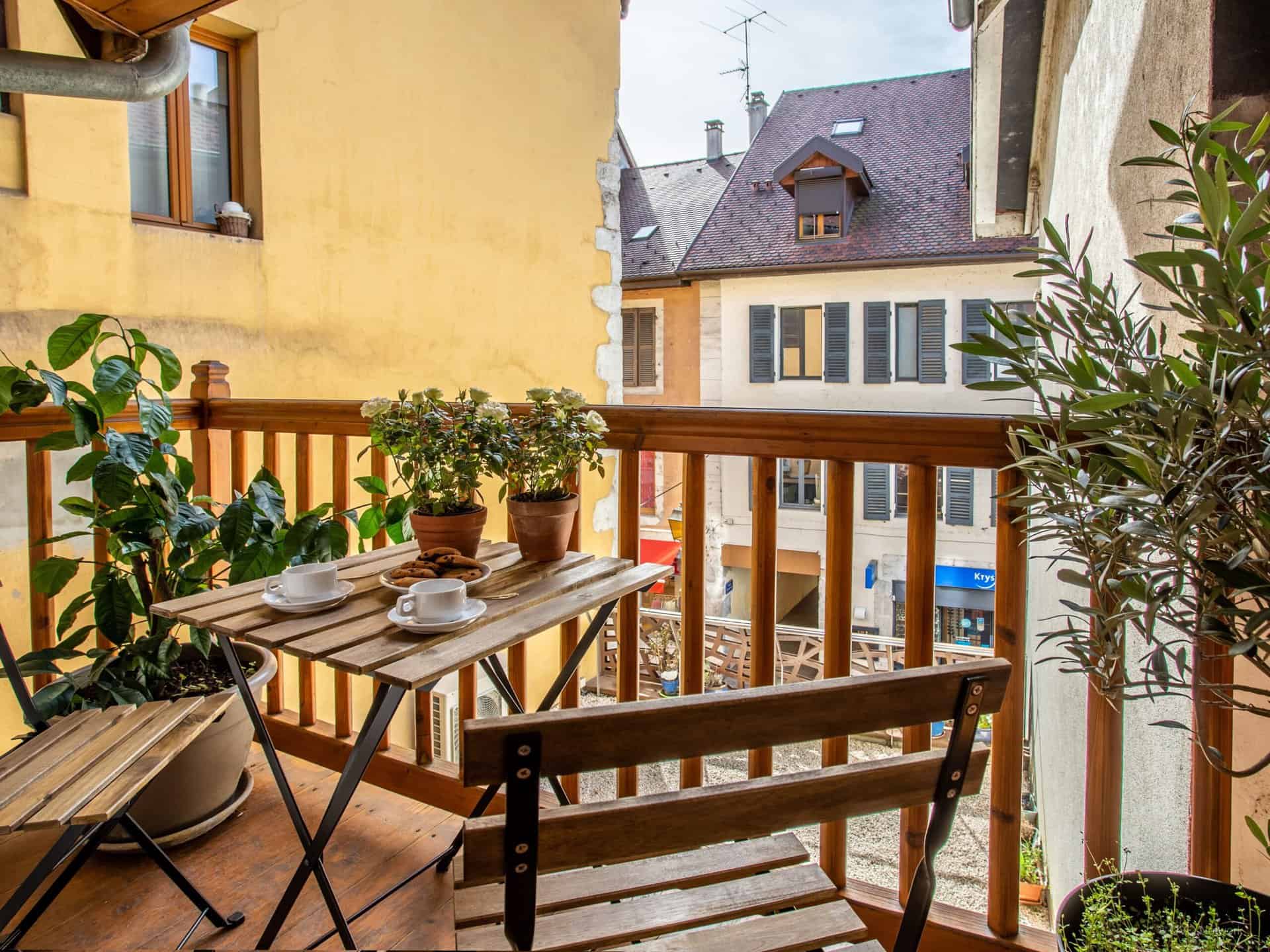 A table and two chairs on the balcony at  Petit SwanDoors, overlooking a street in Annecy.